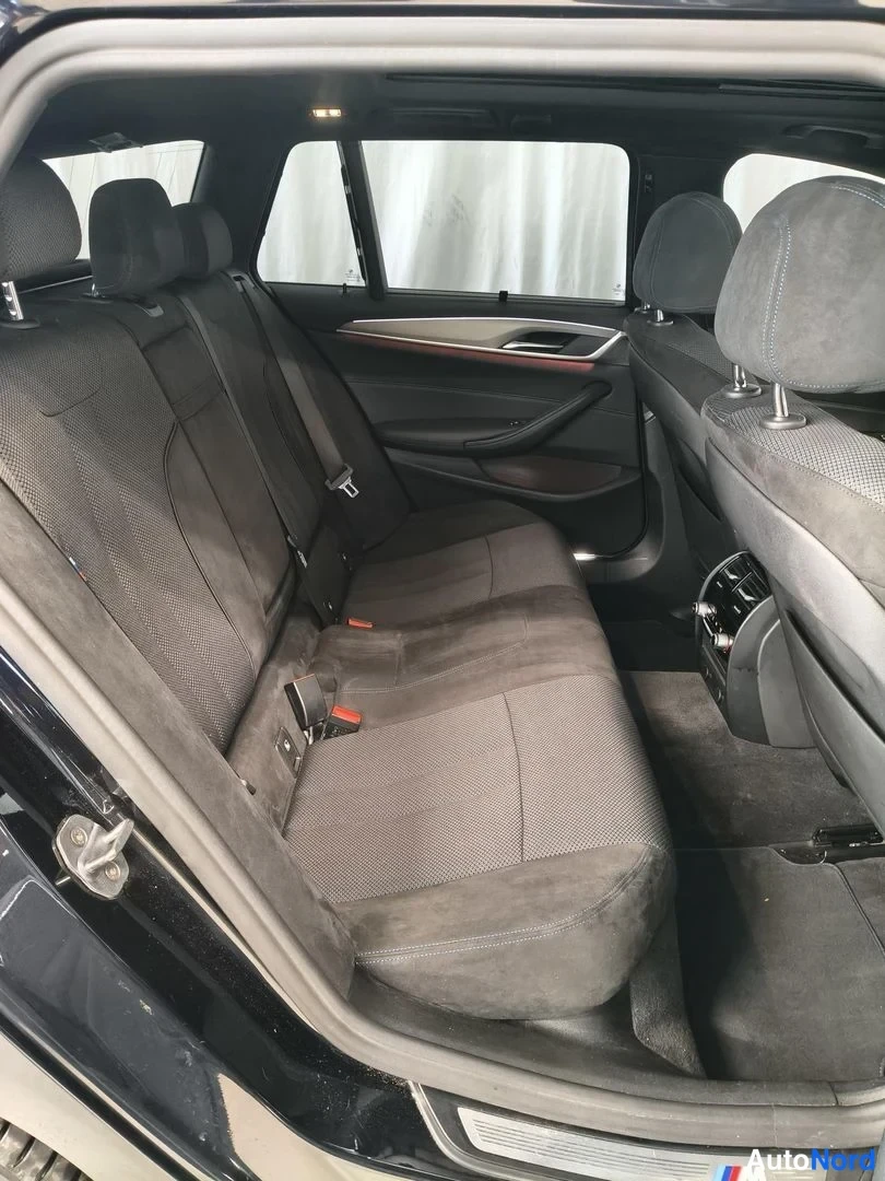 Takaa: Auton takapenkki kuvattuna avoimesta takaluukusta. Tummat kangaspenkit, keskeinen istuin kaikilla kolmella paikalla ja takaa näkyvä panoramic-katon reunat.