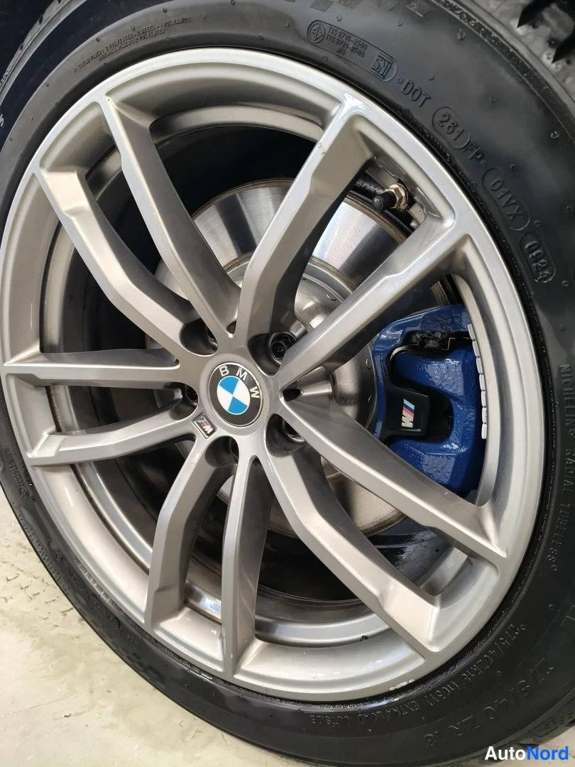 Yksityiskohta: Suljettu kuva BMW:n kevytmetallivanteesta, jossa näkyy sininen M-merkitty jarrusatula ja uritettu jarrulevy.