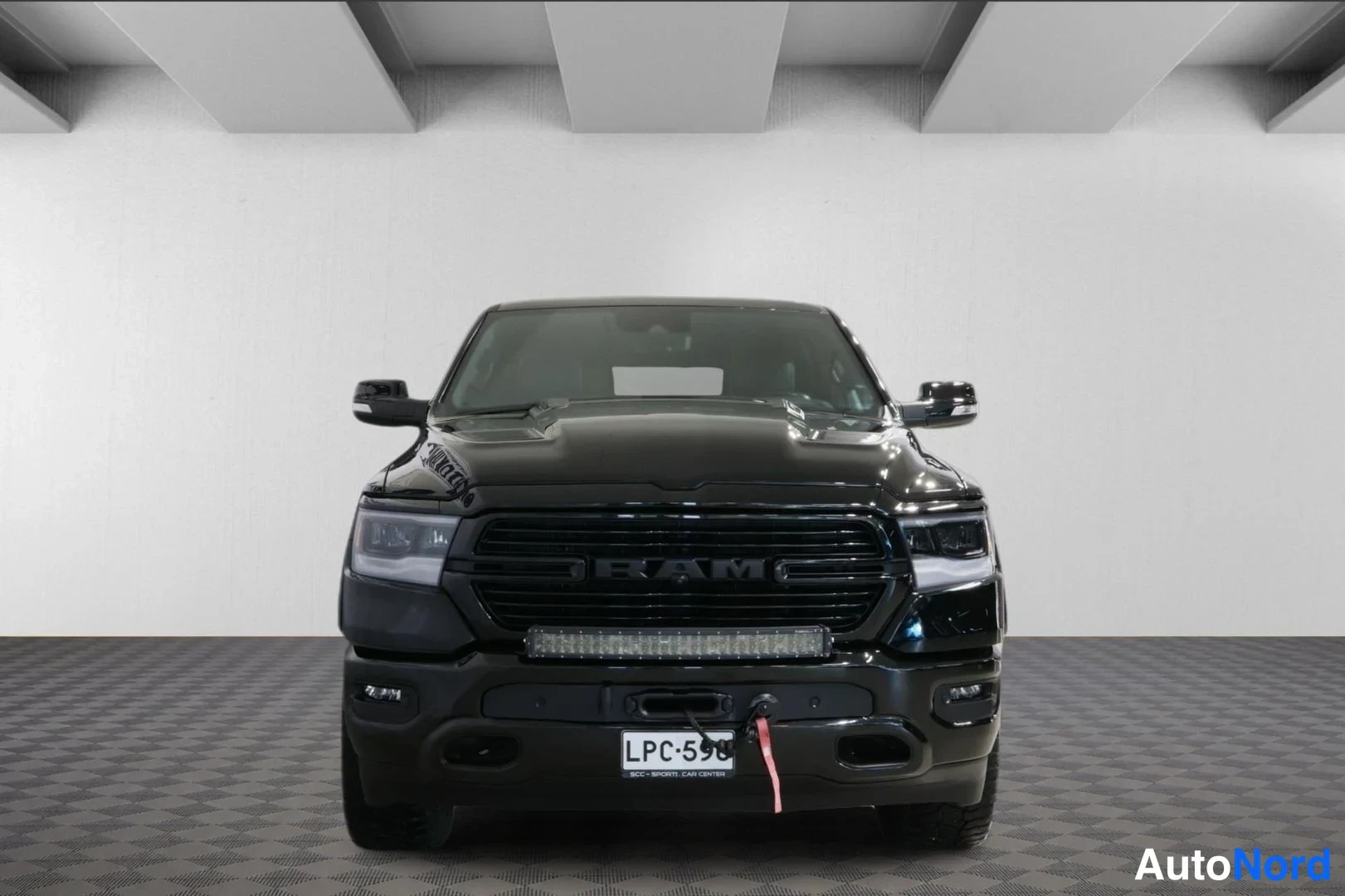 Edestä: Musta Dodge Ram -pickup suoraan edestä, RAM-kyltti säleikkössä ja rekisterikilpi.
