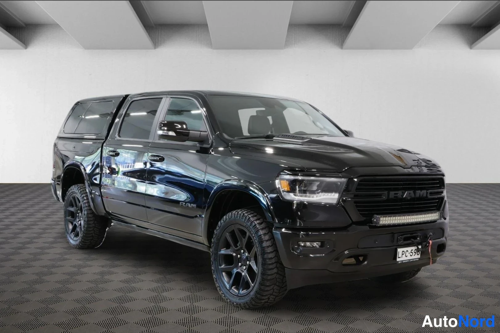 Etuviisto, nokka oikealle: Musta Dodge Ram -pickup etuviistosta oikealle, etuosa ja kylki näkyvissä, rekisterikilpi.