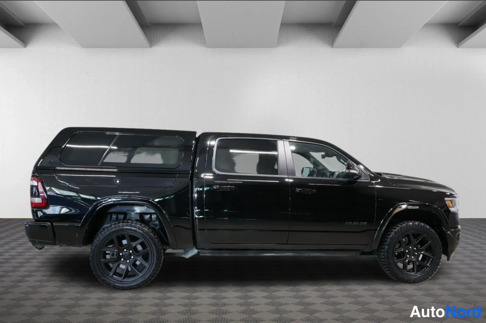 Sivulta: Musta Dodge Ram -pickup kyljeltä neliovisen ohjaamon ja lavalle asennetun kovakannen kanssa.