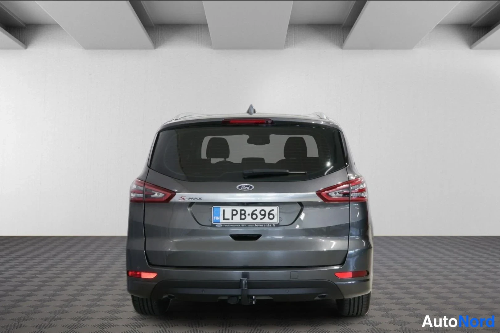 Takaa: Takakulmauskuva hopeanharmaasta Ford S-Max -pakettiautoista, jossa näkyvät takavalot, rekisterinumero ja peräkärrytanko.