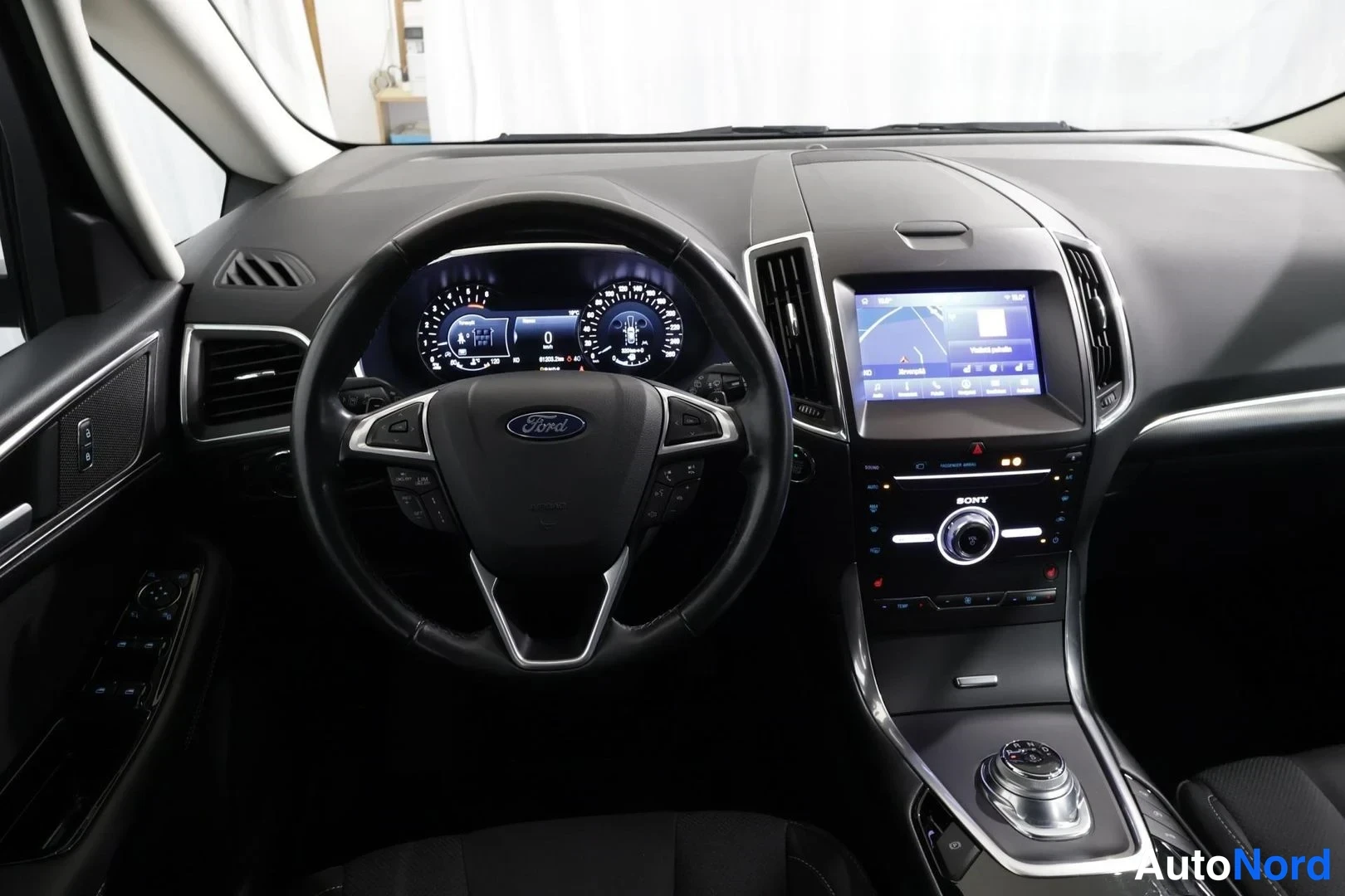 Edestä: Auton ohjaamo ilman kyydissä olevia henkilöitä. Ohjauspyörä ja mittaristo näkyvät, nopeus 0. Ford-tyylinen ohjaamo, navinäyttö ja radio (Sony) keskikonsolissa.