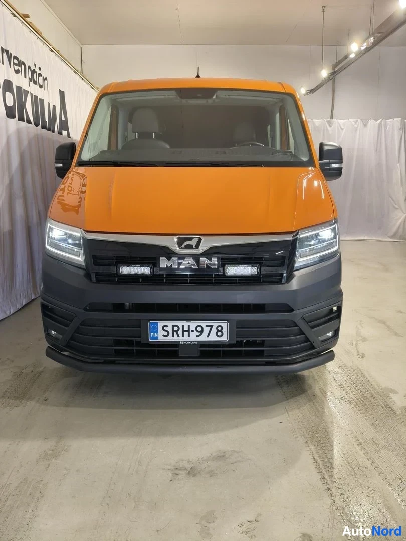 Edestä: MAN TGE -pakettiauto suoraan edestäpäin kuvattuna, oranssi kori ja musta etusarja, rekisterikilpi.