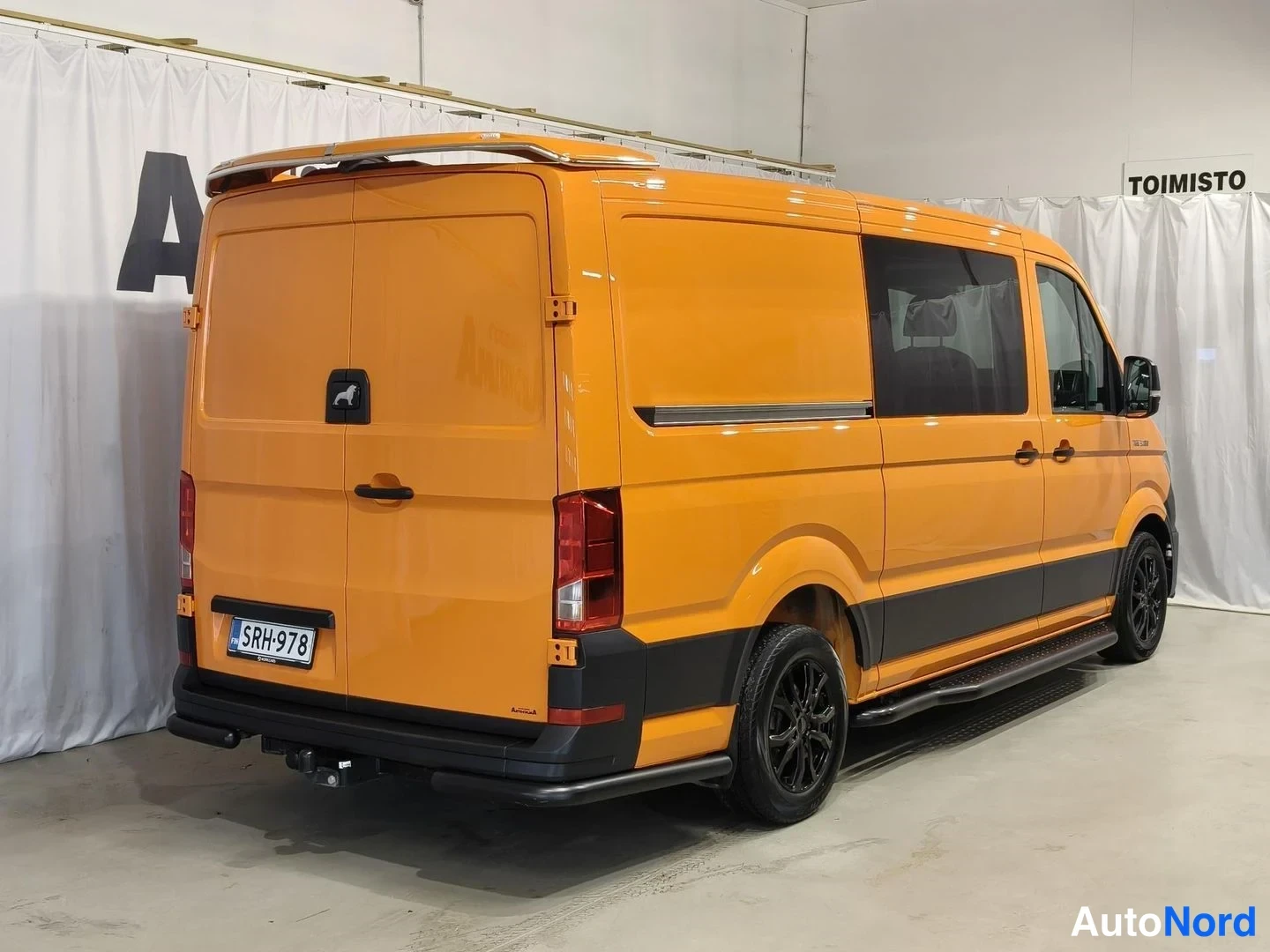 Takaviisto: MAN TGE -pakettiauto takaa vasemmalta, oranssi kori, rekisterikilpi ja mustat vanteet.