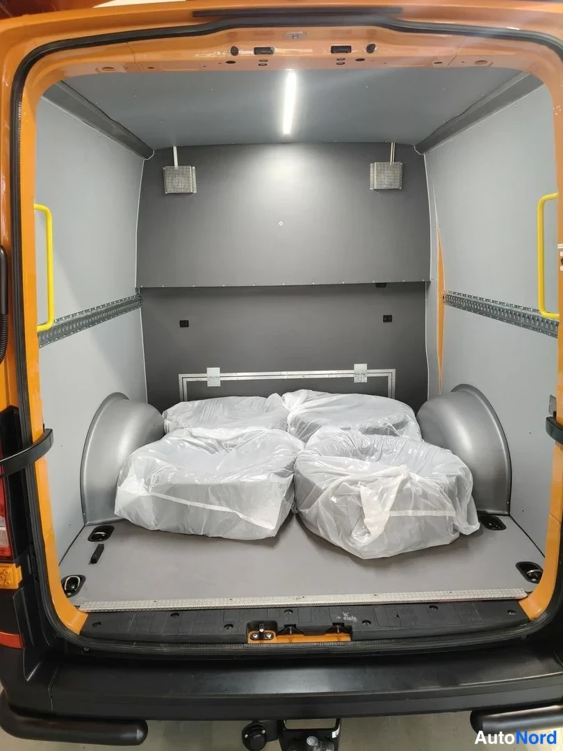 Takaa: Pakettiauton takaosan avattu lastitila: oranssit runkopaneelit, harmaa lattia ja seinät, kattovalo ja muovipusseissa olevia osia.