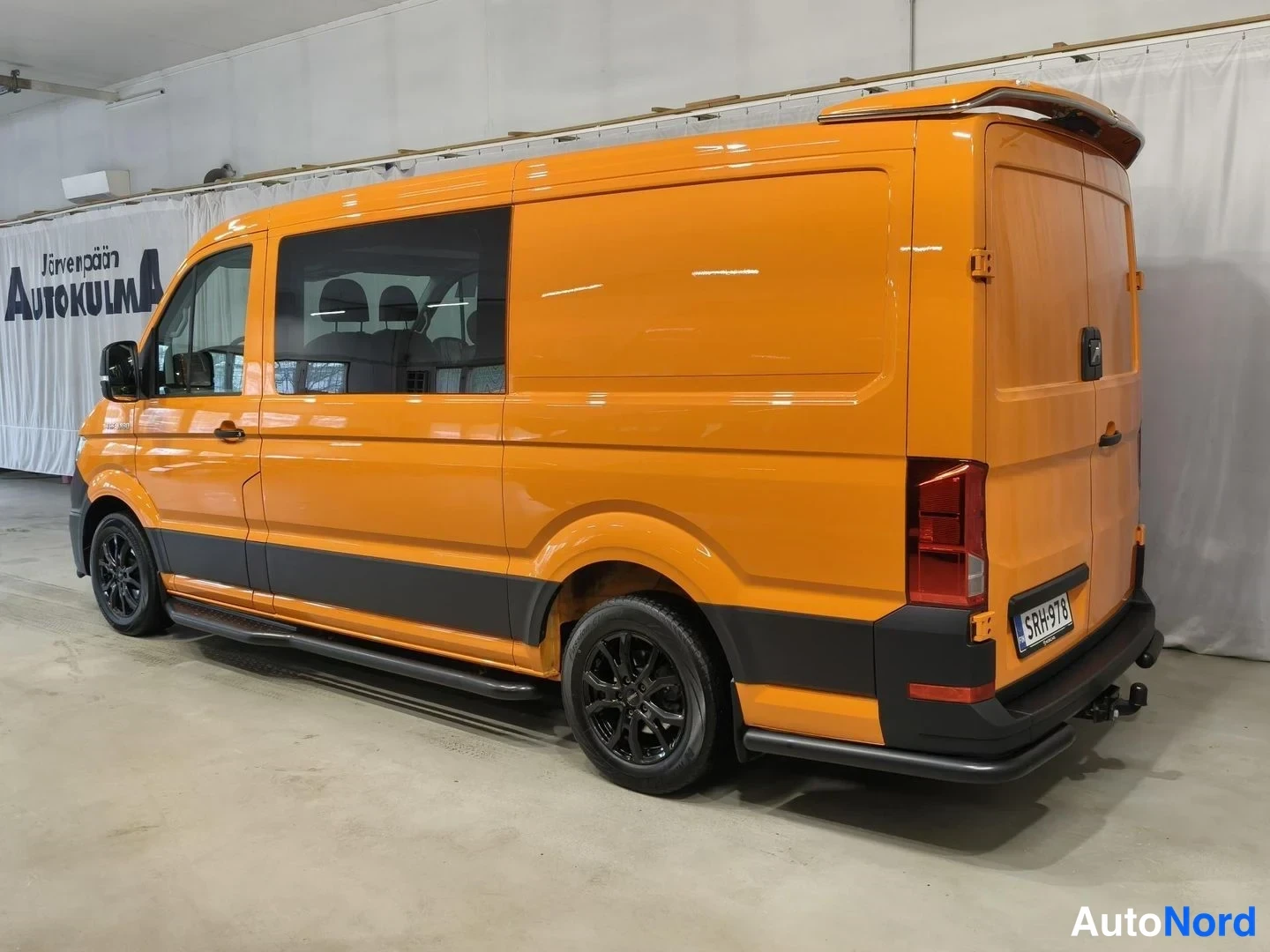 Takaviisto: Oranssi pakettiauto takaviistosta kuvattuna sisätiloissa, rekisterikilpi