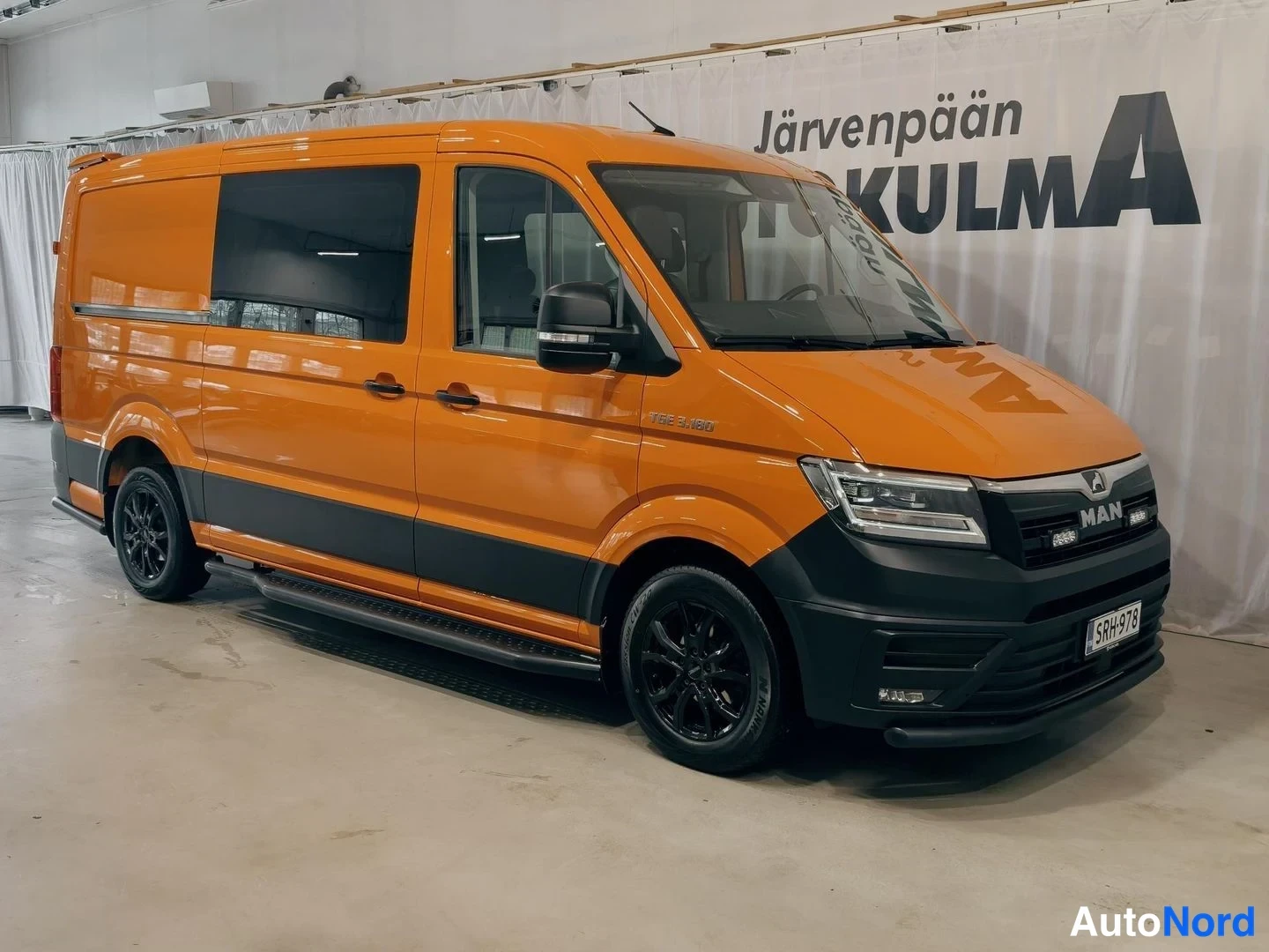 Etuviisto, nokka oikealle: Oranssi pakettiauto etuviistosta oikealta kuvattuna sisätiloissa, rekisterikilpi