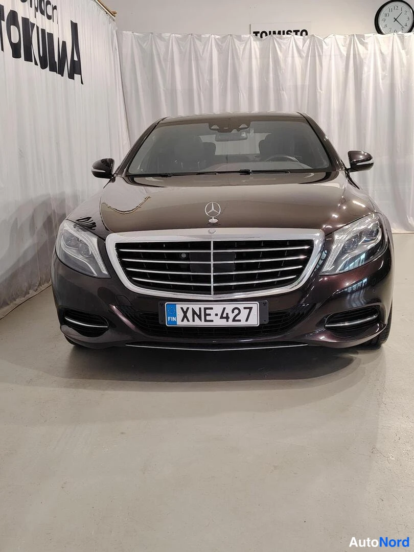 Edestä: Mercedes-Benz S-luokan sedan suora etäkuva tummanpunaisella maalilla. Kromilattinen jäähdytinta-fasadi ja Mercedes-tähtimerkki konepellissä, rekisterikilpi.