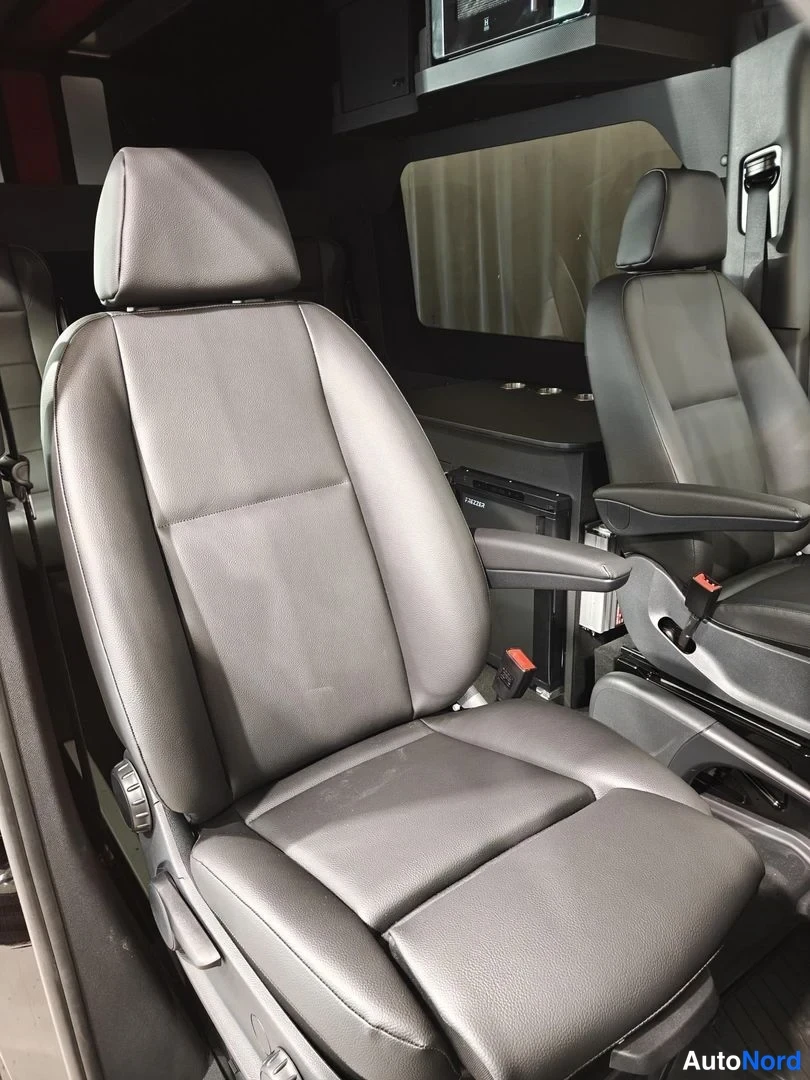 Muu: Musta nahkaverhoiltu etumatkustajan istuin autocamper-mallisessa Mercedes-Benz Sprinter -pakettiauton sisätilassa, takana toinen istuin ja tumma kaapisto.