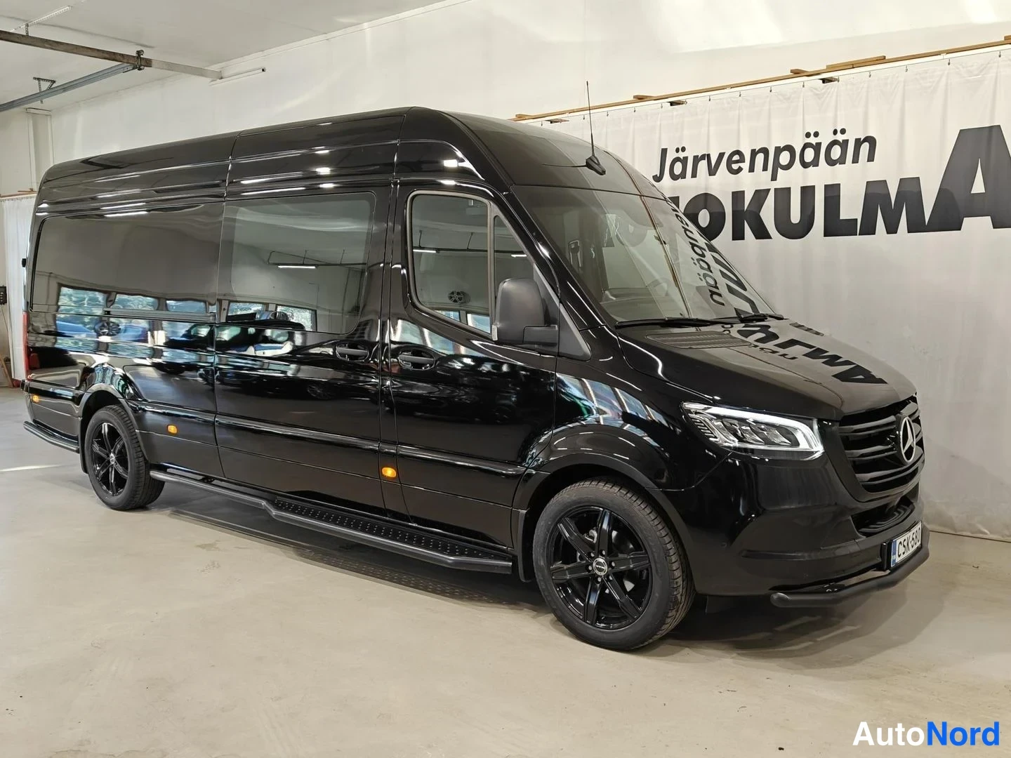 Etuviisto, nokka oikealle: Musta Mercedes-Benz Sprinter -pakettiauto kuvattu kolmikonäkymässä edestä oikealta sisätilassa, sivulla askelma.
