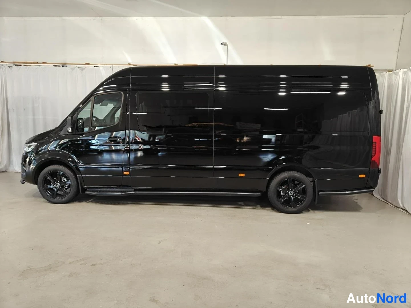 Sivulta: Musta Mercedes-Benz Sprinter -pakettiauto vasemman puolen profiilissa. Mustat kevytmetallivanteet ja sivujalustat näkyvät.