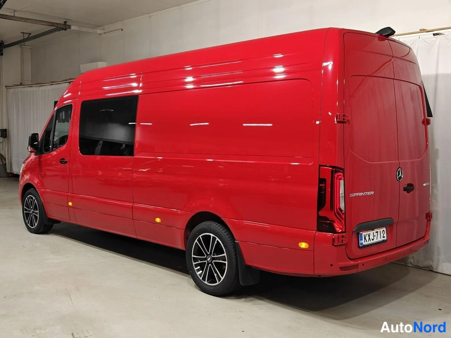 Takaviisto: Punainen Mercedes-Benz Sprinter -pakettiauto takaviistosta sisätiloissa, Sprinter-teksti takaovessa ja rekisterikilpi.