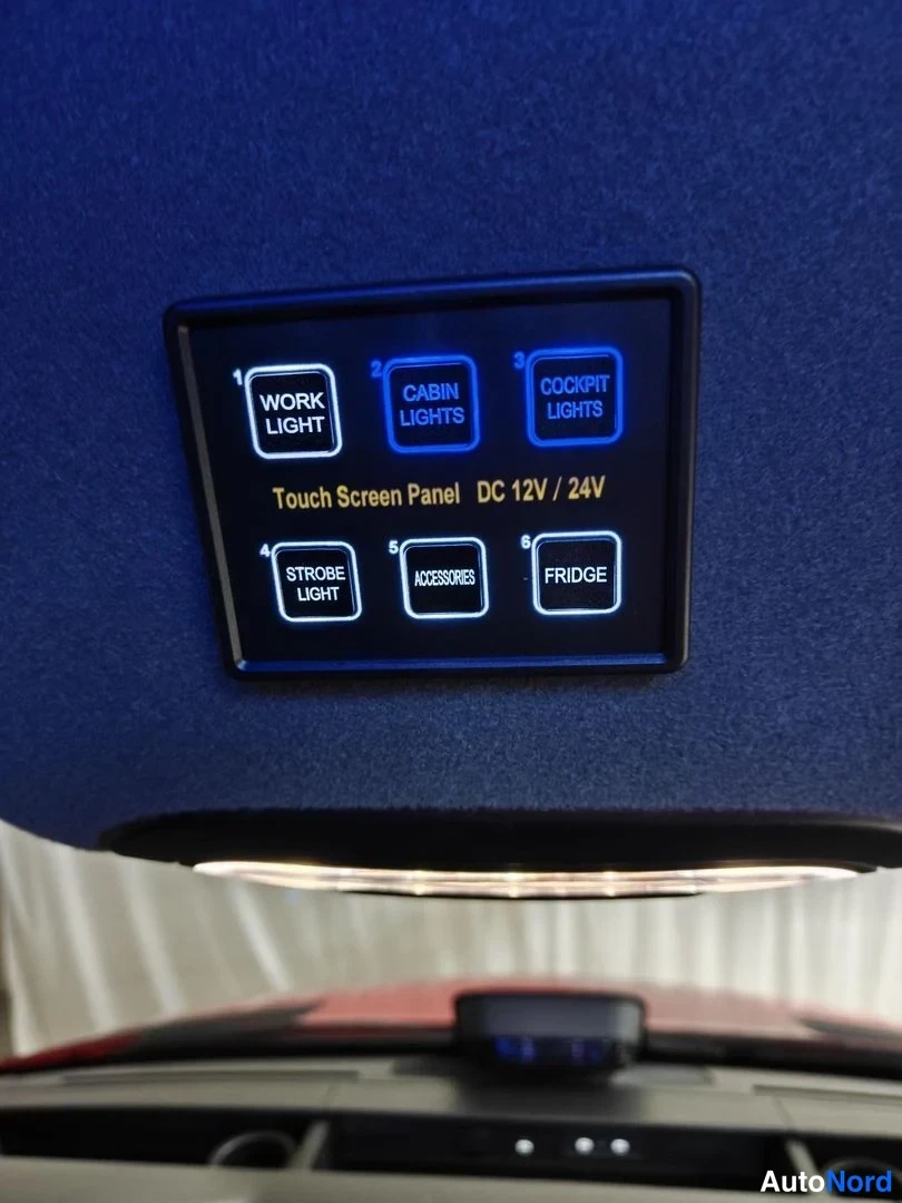 Sivulta: Kattopaneeliin asennettu kosketusnäyttöpaneeli: painikkeet WORK LIGHT, CABIN LIGHTS, COCKPIT LIGHTS, STROBE LIGHT, ACCESSORIES ja FRIDGE sekä teksti Touch Scree