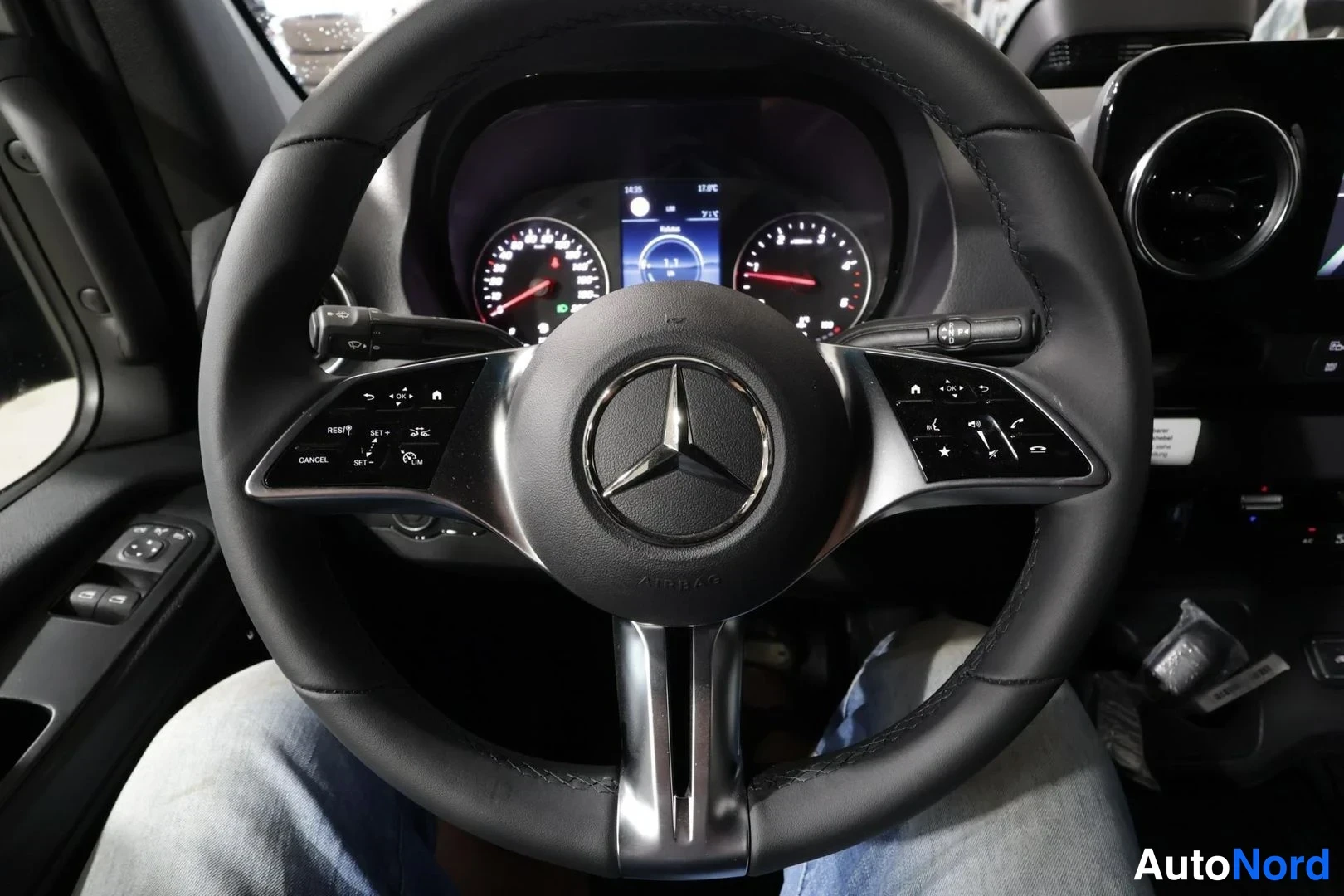 Yksityiskohta: Mercedes-Benzin ohjauspyörä tähtimerkillä, monitoiminäppäimet molemmin puolin ja takana digitaalinen mittaristo nopeusmittarilla ja kierrosmittarilla.