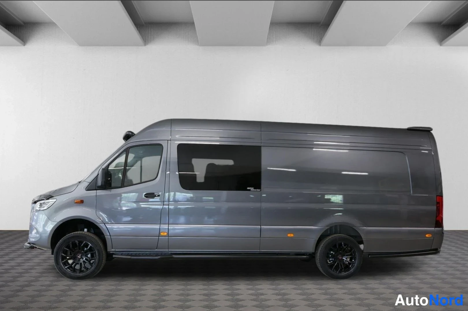 Sivulta: Sivulta kuvattu tummanharmaa pitkä Mercedes-Benz Sprinter -pakettiauto, tummat kevytmetallivanteet ja sivuluisut, peitetyt takasivuikkunat.