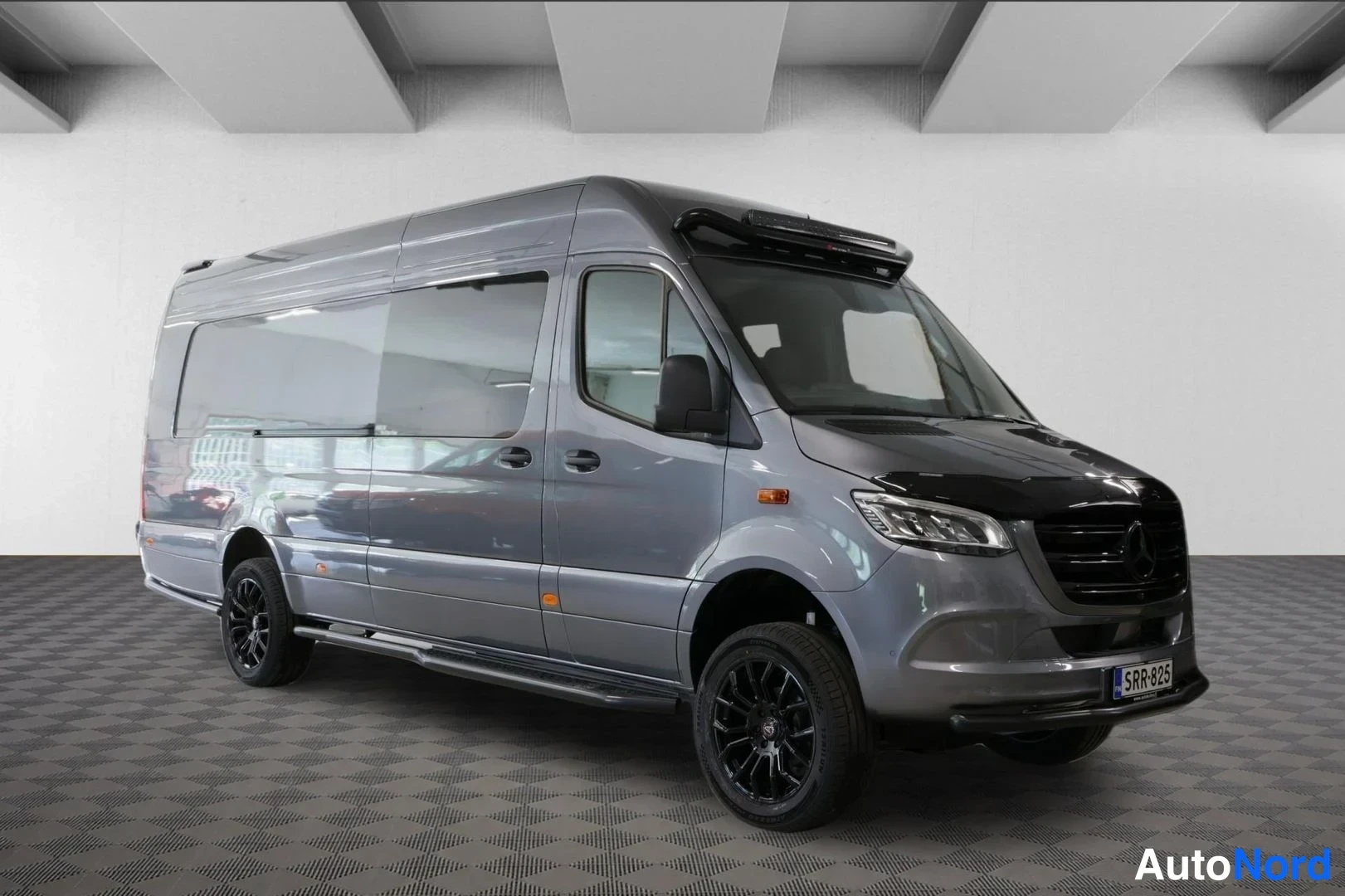 Etuviisto, nokka oikealle: Etukulmasta oikealta kuvattu tummanharmaa Mercedes-Benz Sprinter -pakettiauto, mustat vanteet, kattotelineet ja rekisterikilpi.