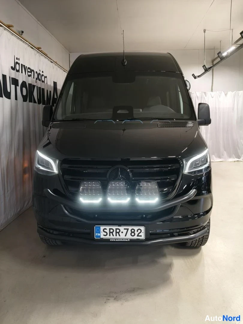 Edestä: Mercedes-Benz Sprinter -pakettiauto edestä kuvattuna, musta, lisävalot etupuskurissa, rekisteritunnus.