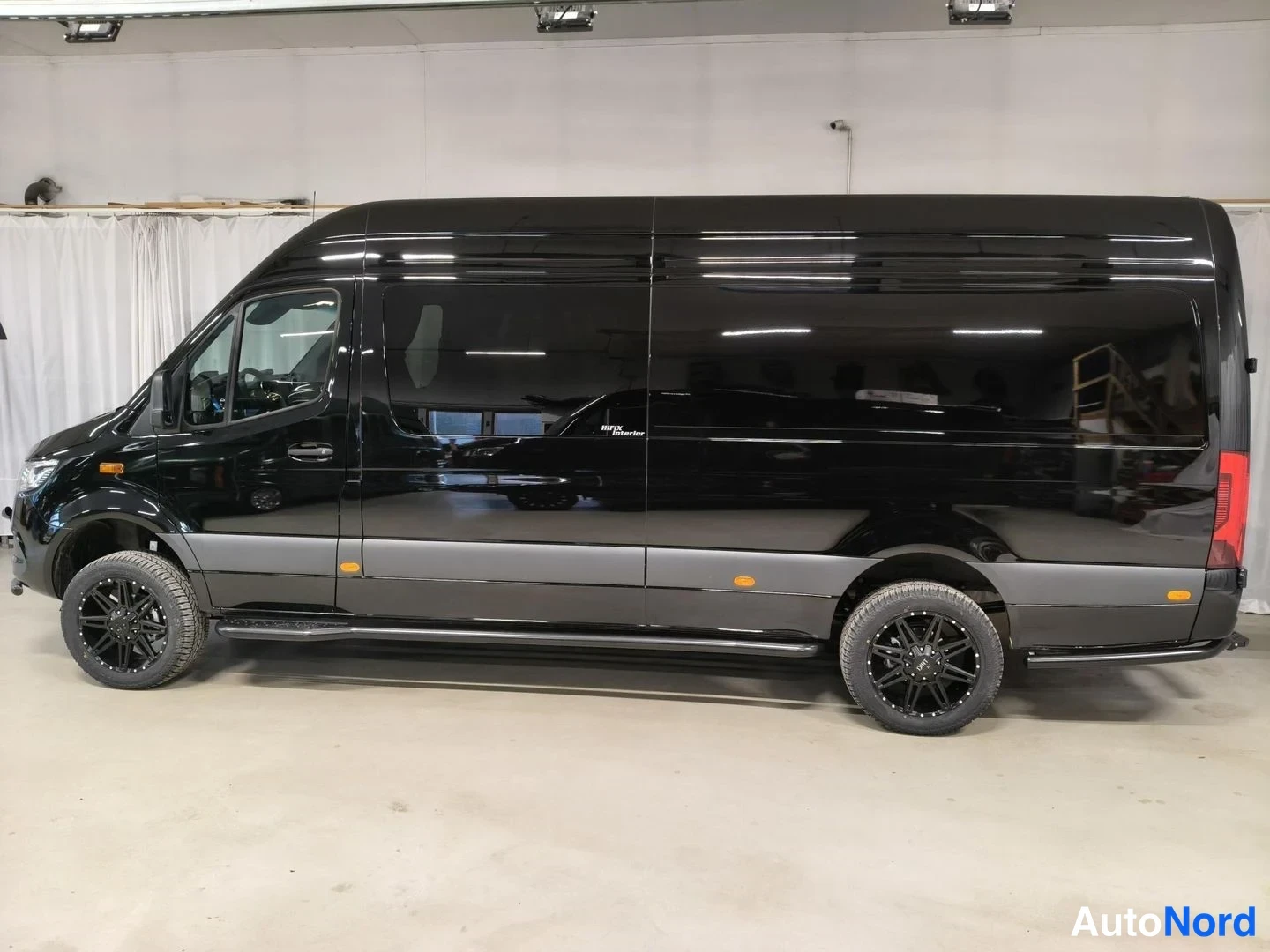 Etuviisto, nokka vasemmalle: Musta Mercedes-Benz Sprinter -pakettiauto sivulta kolmasosa-kulmassa keula vasemmalla, mustat vanteet ja kromilistat, sisätiloissa valkoinen tausta.