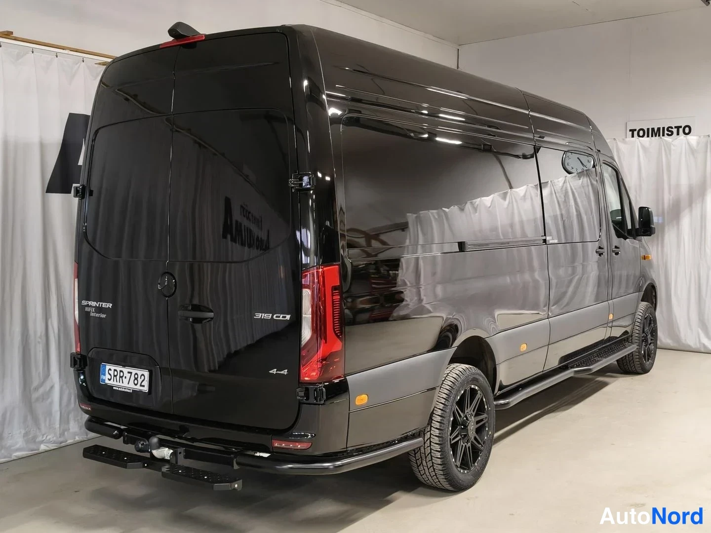 Takaviisto: Musta Mercedes-Benz Sprinter 319 CDI 4x4 -pakettiauto takaviistosta kuvattuna sisätilassa.