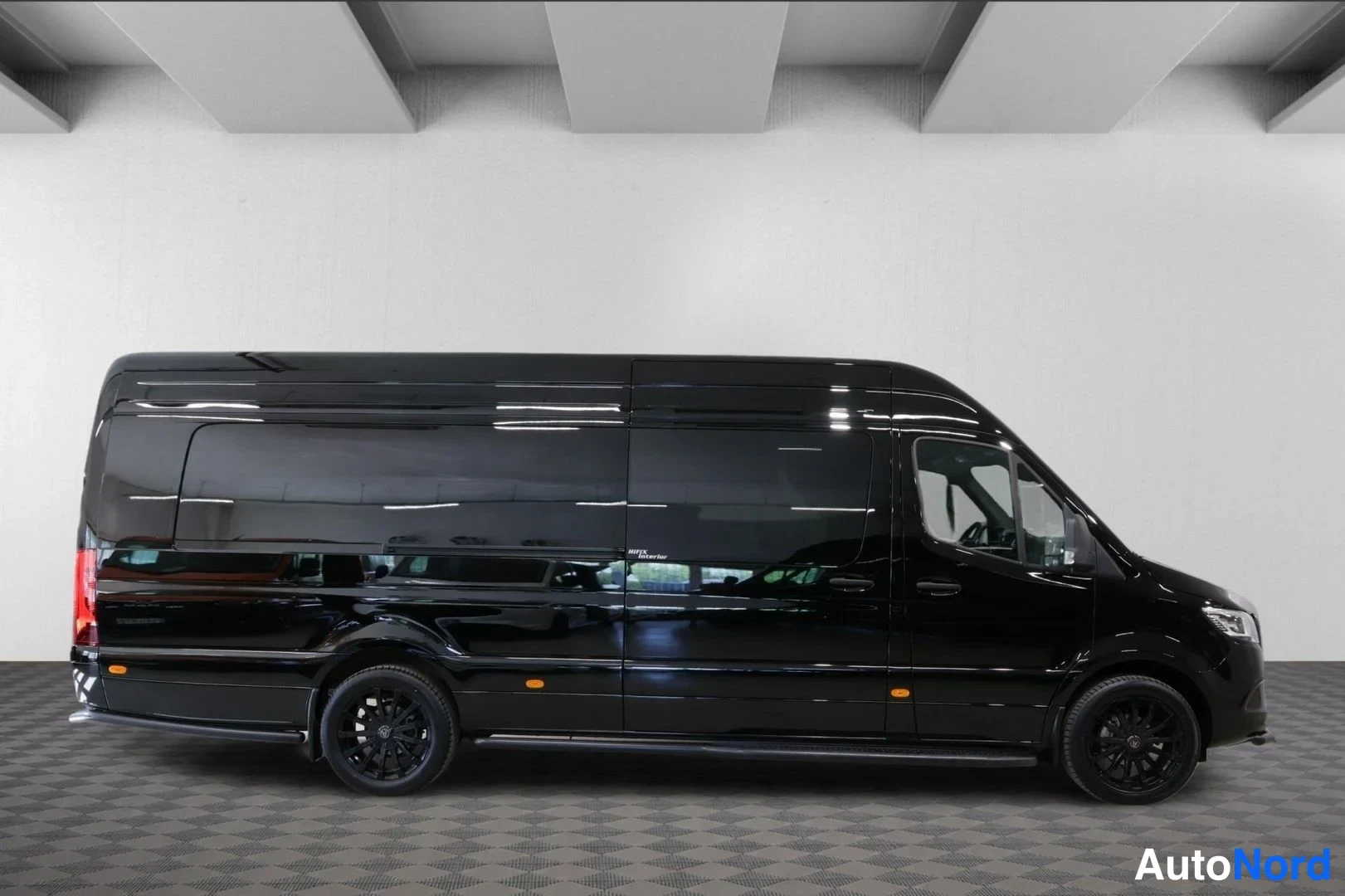 Sivulta: Musta Mercedes-Benz Sprinter -pakettiauto sivulta, pitkä korimalli ja tummat vanteet näkyvissä.