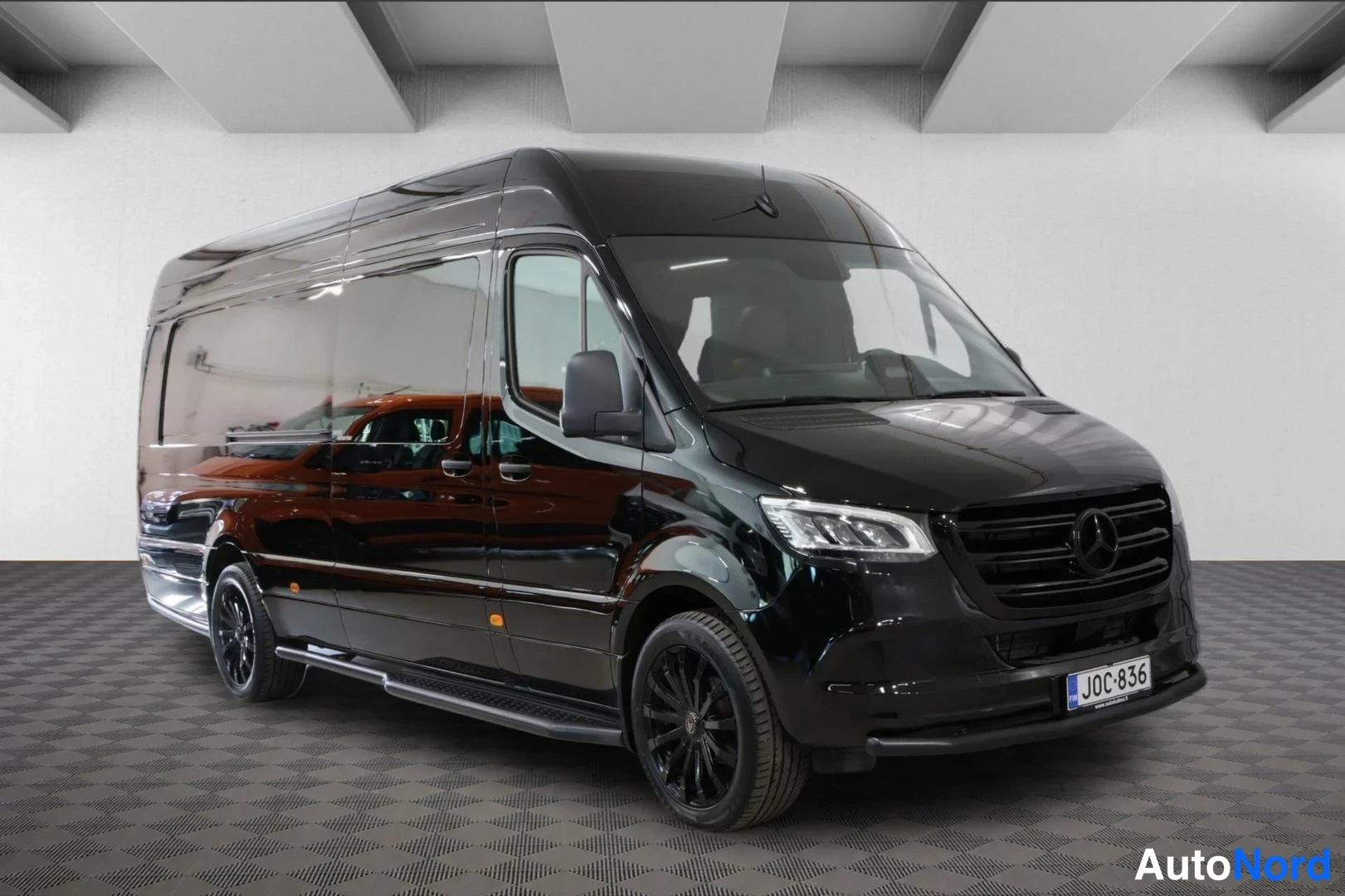Etuviisto, nokka oikealle: Musta Mercedes-Benz Sprinter -pakettiauto edestä viistosta, tumma etusäleikkö ja mustat vanteet näkyvissä.