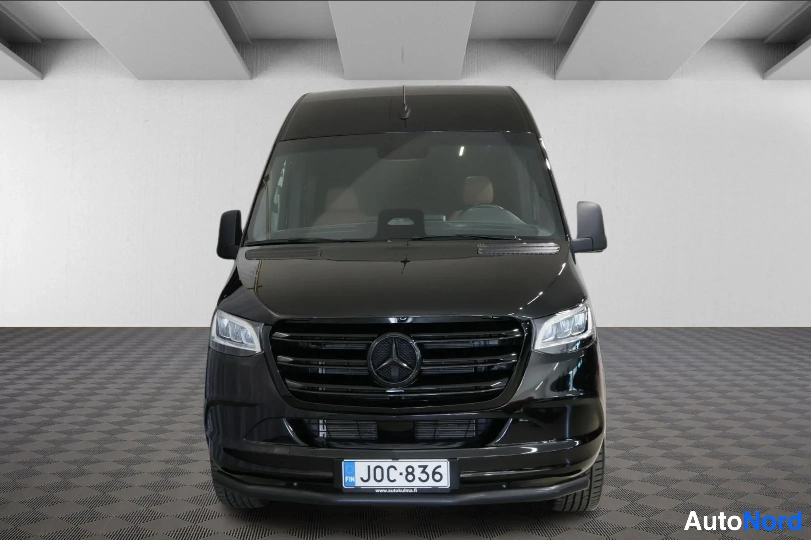 Edestä: Musta Mercedes-Benz Sprinter -pakettiauto suoraan edestä, tumma etusäleikkö ja rekisterikilpi näkyvissä.