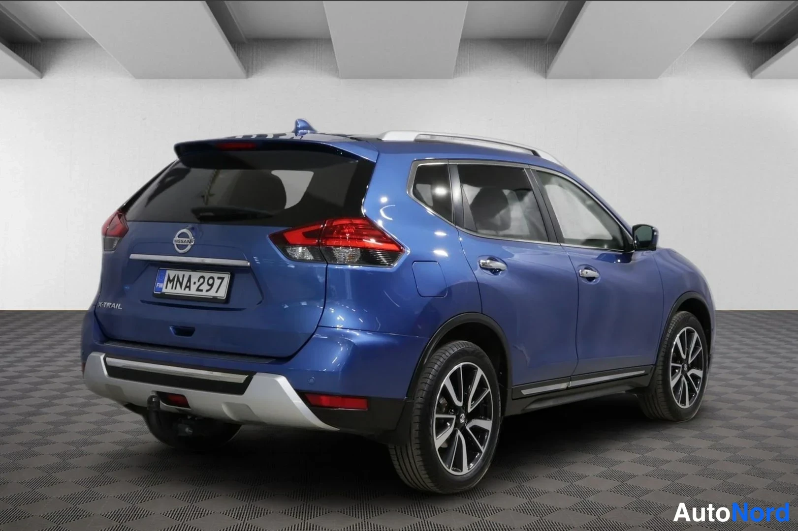 Takaviisto: Sininen Nissan X-Trail -maasturin takaosa ja oikea kylki näkyvät kolmasosakulmassa; hopeiset kattokaiteet ja vetokoukku. Rekisterikilpi.
