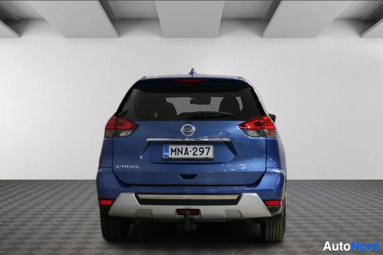 Takaa: Nissan X-Trailin takanäkyvissä rekisterikilpi ja X-Trail-teksti, autotallin harmaata lattiaa vasten.