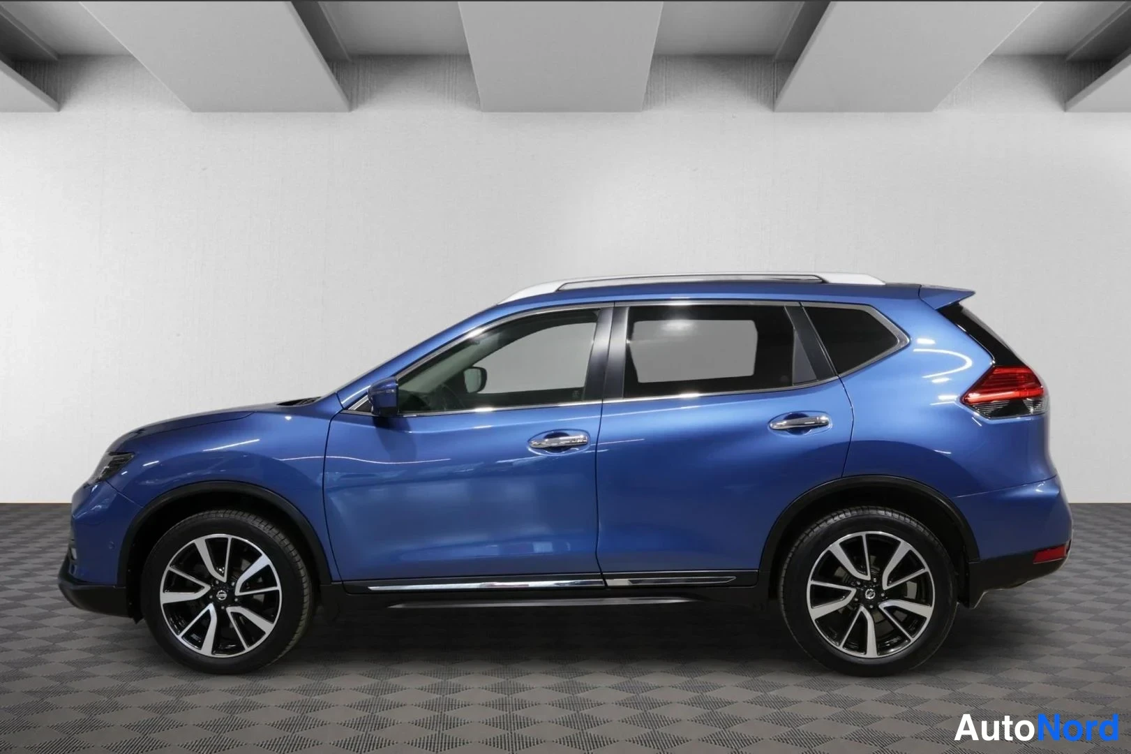 Sivulta: Sivukuvassa sininen Nissan X-Trail, hopeiset ovikoristeet, kattokaiteet ja tummat kevytmetallivanteet.