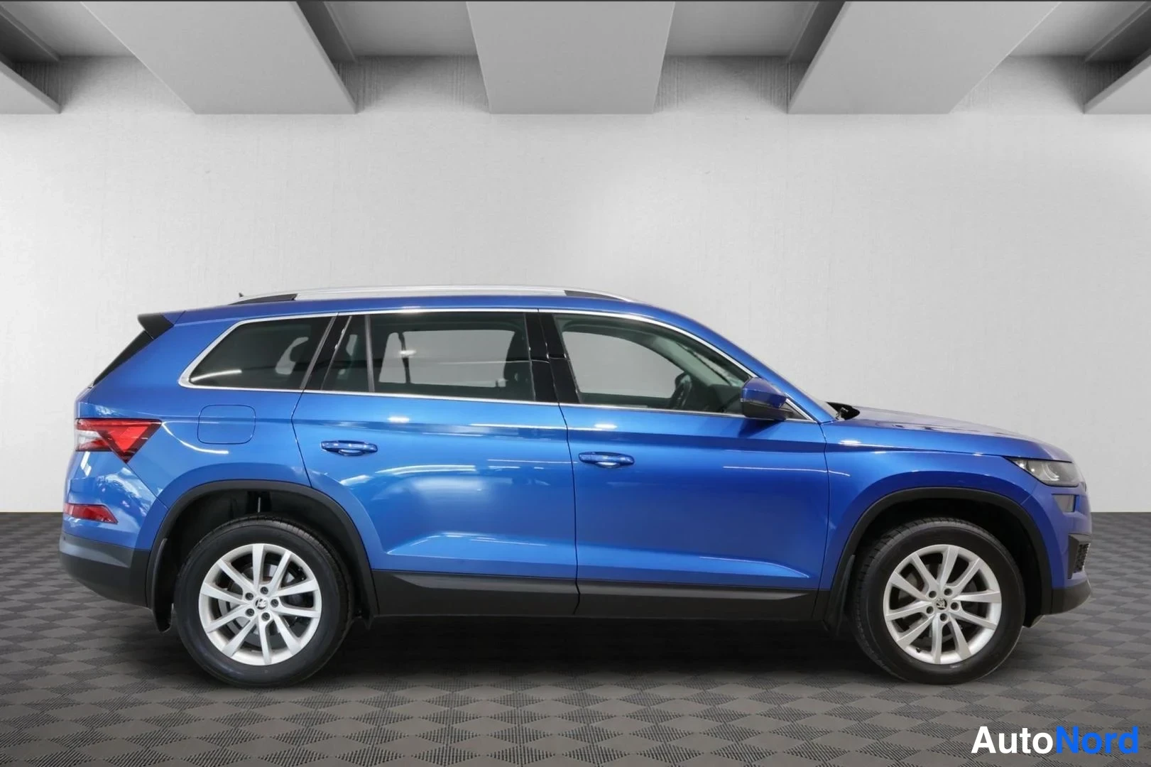 Takaviisto: Sivuprofiili sinisestä Skoda Kodiaq -SUV:sta studioympäristössä, takavalojen ja etupään ääriviivat näkyvissä.