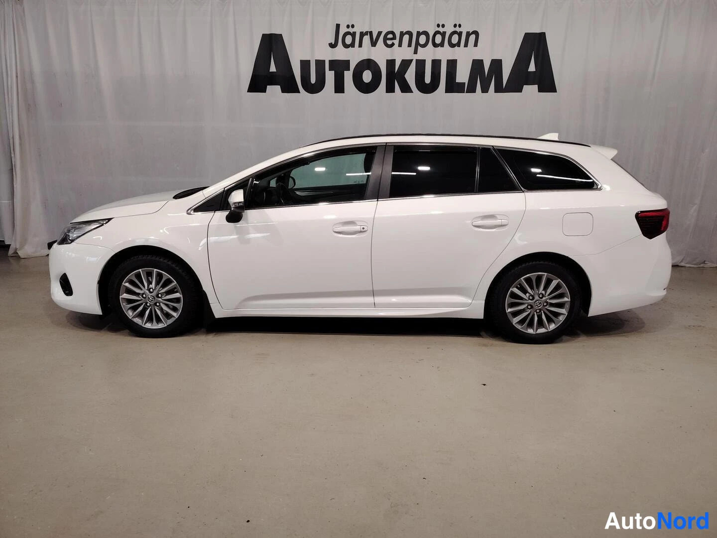 Etuviisto, nokka vasemmalle: Sivukulma: valkoinen farmariauto vasemmasta sivusta kuvattuna, etukyhä ja etuvalo näkyvät kuvan vasemmassa reunassa.