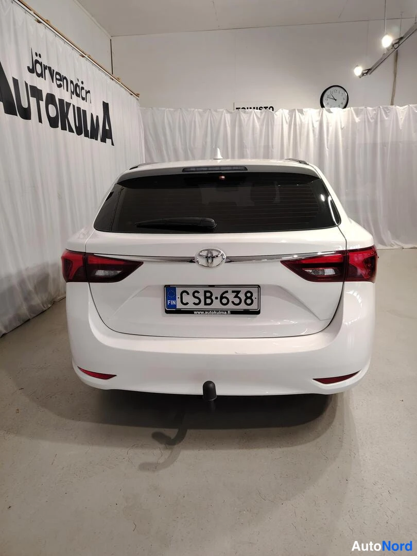 Takaa: Takakulma: valkoisen farmariauton takaosa suoraan takaa, Toyota-merkki ja rekisterikilpi näkyvät.