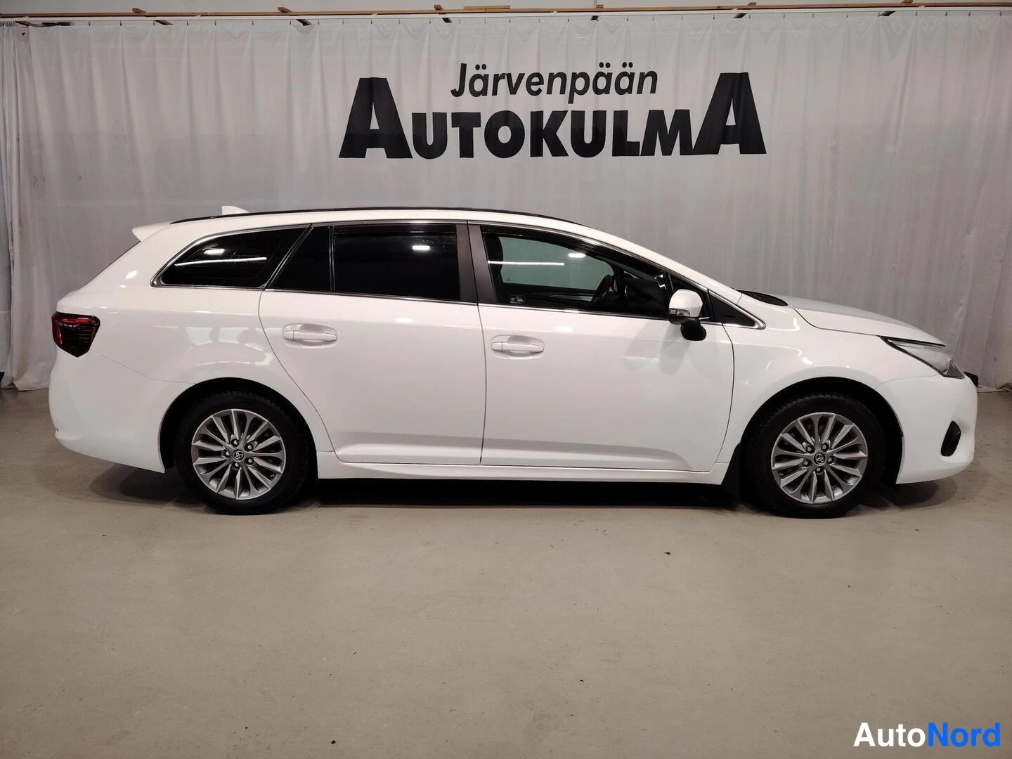 Takaviisto: Takakolmasosa: valkoinen farmariauto kuvattuna takaosasta ja vasemmalta sivulta, takavalot näkyvät kuvan vasemmassa reunassa.