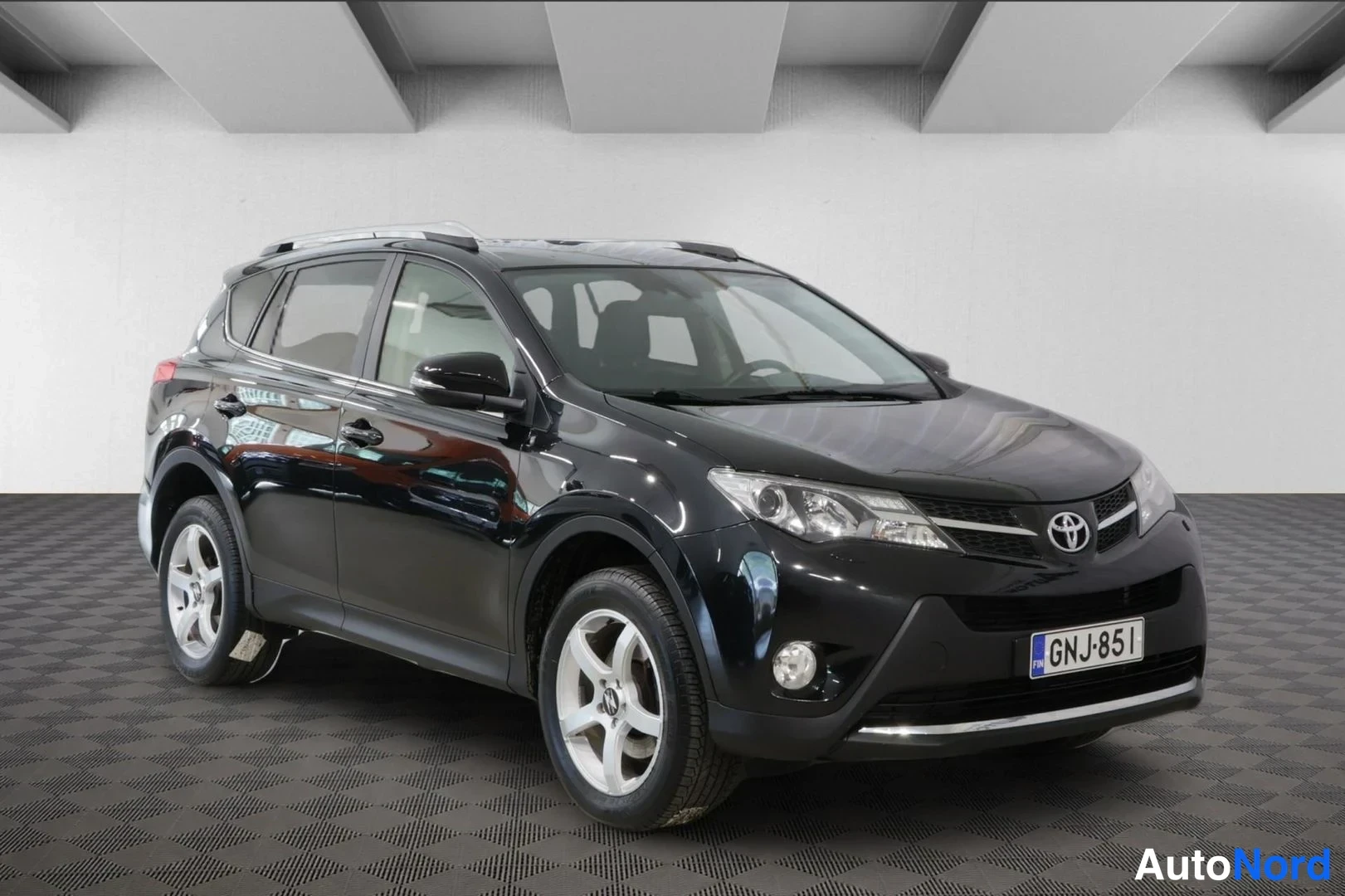 Etuviisto, nokka oikealle: Musta Toyota RAV4 etuviistosta oikealta; keulalla Toyota-merkki, sumuvalot ja rekisterikilpi, kattotelineet päällä.