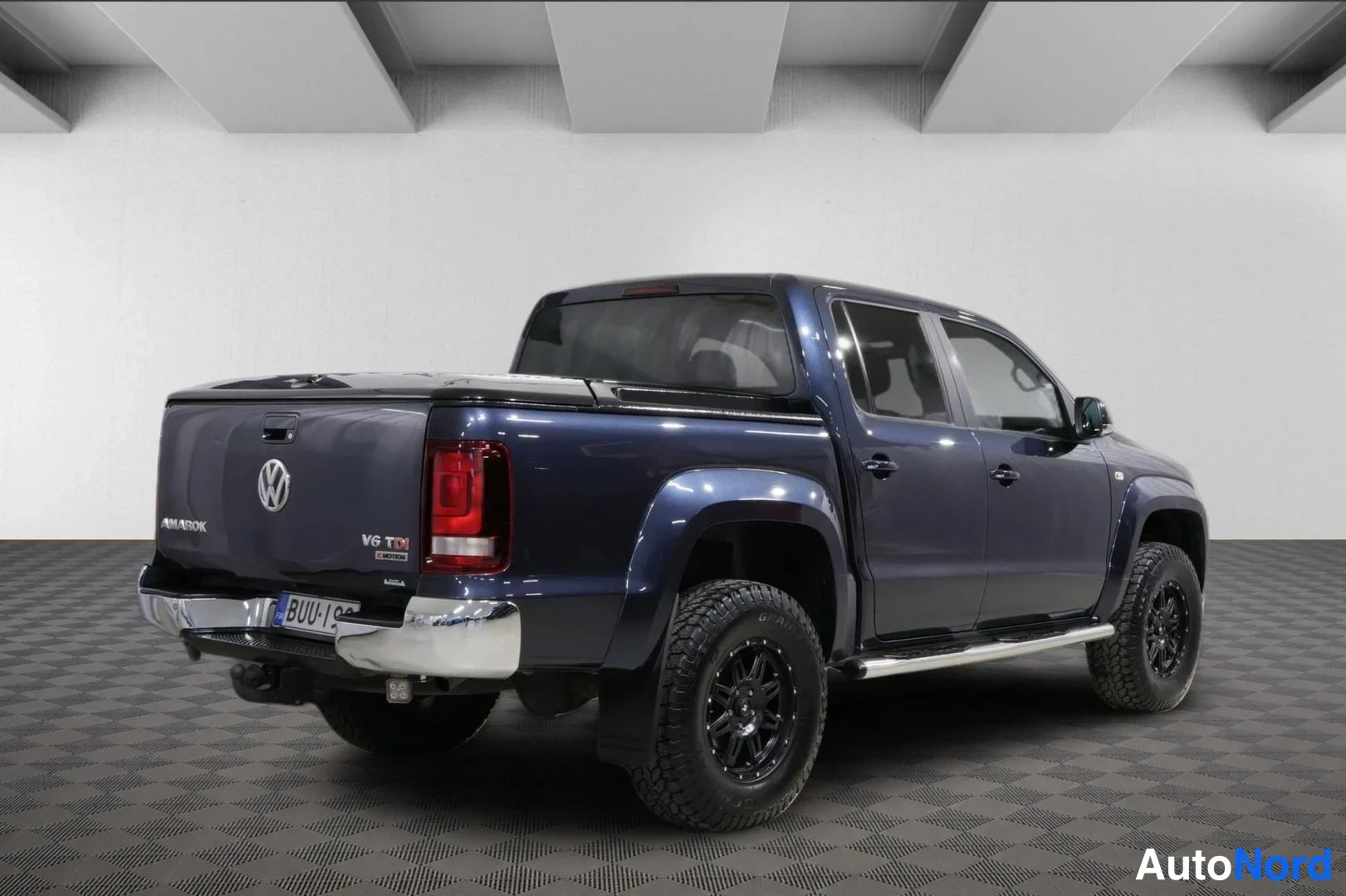 Takaviisto: Tummansinisen Volkswagen Amarok -lava-auton takaosan kolmasosan kuva oikealta, takavalot ja laveerattu lavakansi näkyvät.