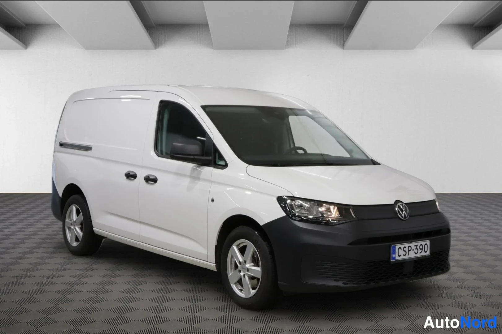 Etuviisto, nokka oikealle: Valkoinen Volkswagen Caddy -pakettiauto etuviistosta oikealta, musta etupuskuri ja rekisteritunnus.