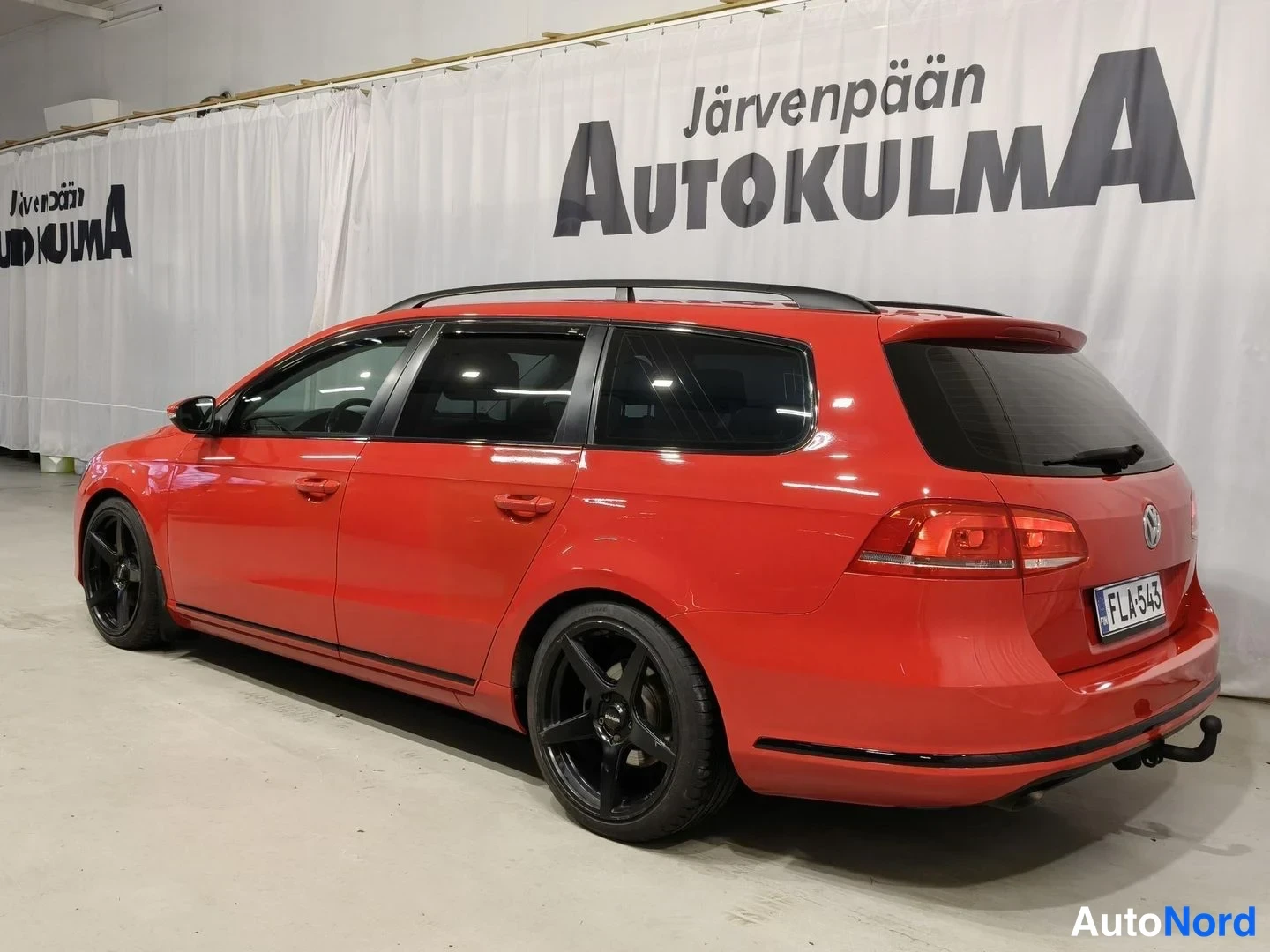 Takaviisto: Punainen farmariauto takaviistosta, rekisterikilpi, mustat vanteet ja kattotelineet.