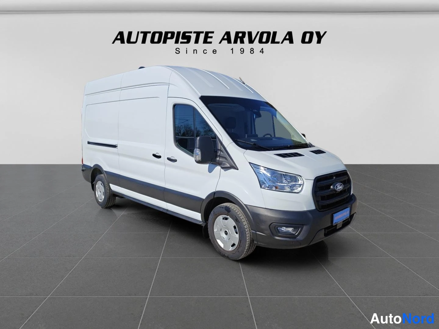 Etuviisto, nokka oikealle: Valkoinen Ford Transit -pakettiauto kulmassa kuvattuna niin, että keula ja vasen sivu näkyvät; studiovaalea tausta ja lattia, taustalla teksti 'AUTOPISTE