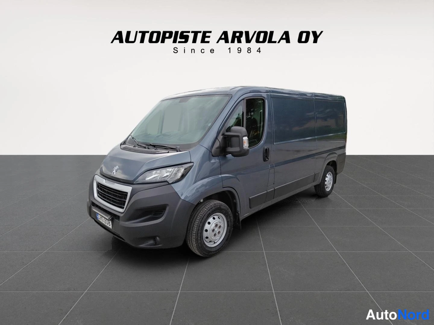 Etuviisto, nokka vasemmalle: Tummanharmaa Peugeot Boxer -pakettiauto etukulmasta, keula vasemmalla, laaja sivunäkymä ovista ja takapyörästä.
