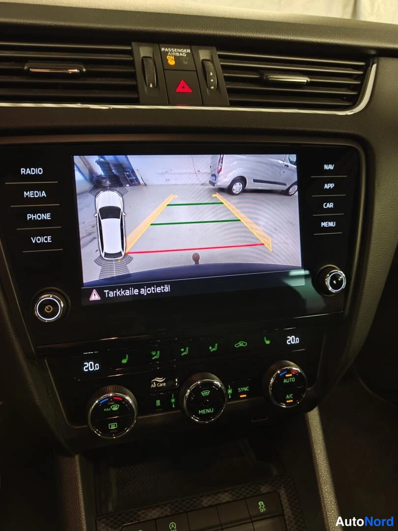 Yksityiskohta: Keskusnäyttö näyttää peruutuskameran kuvan ohjausviivoineen ja varoituksen 'Tarkkaile ajotietä!'; alla automaattisen ilmastoinnin säätimet (20.0°, AUTO, A/C).