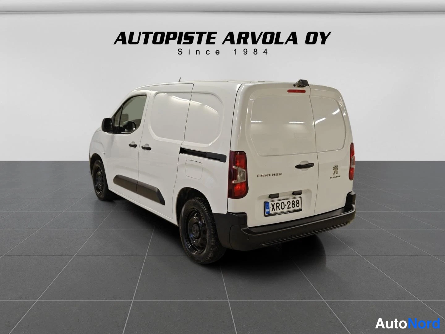 Takaviisto: Peugeot Partner takaosa vinosti oikealta valkoinen pakettiauto, takovitet Partner-logo ja rekisterikilpi.