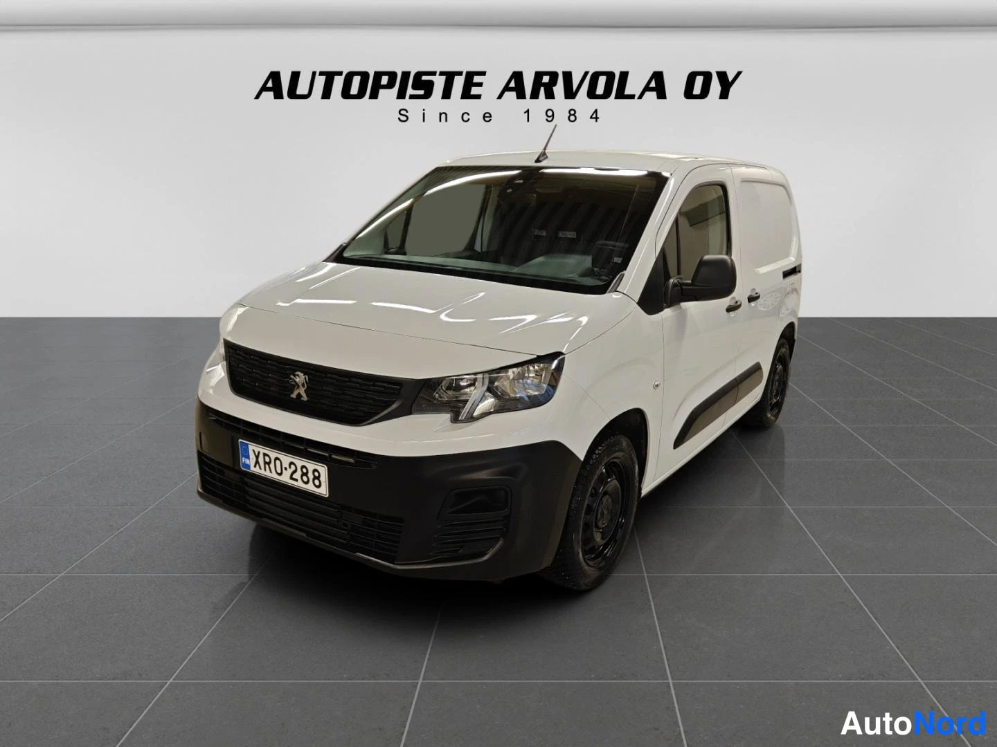 Etuviisto, nokka vasemmalle: Peugeot Partner etuosa vinosti vasemmalta valkoinen pakettiauto studiovalaistuksessa.