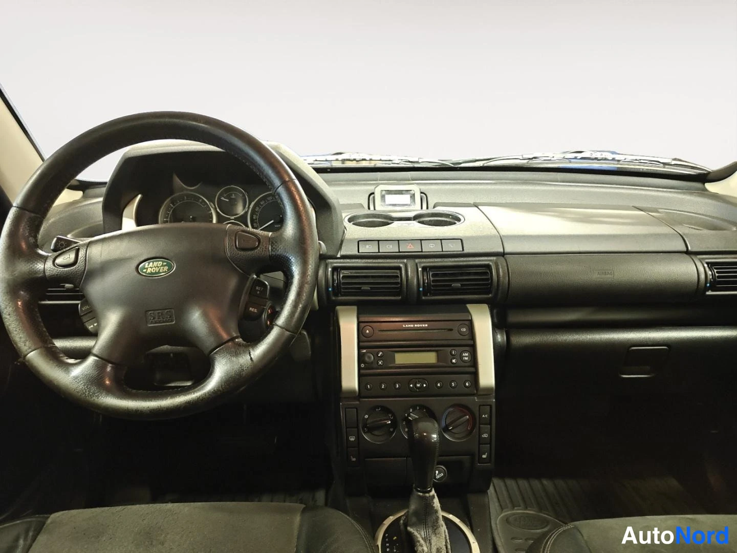 Edestä: Ohjaamo Land Rover Freelander -merkillä: ohjauspyörä, kojelauta, radio ja automaattivaihteen vaihdekeppi.