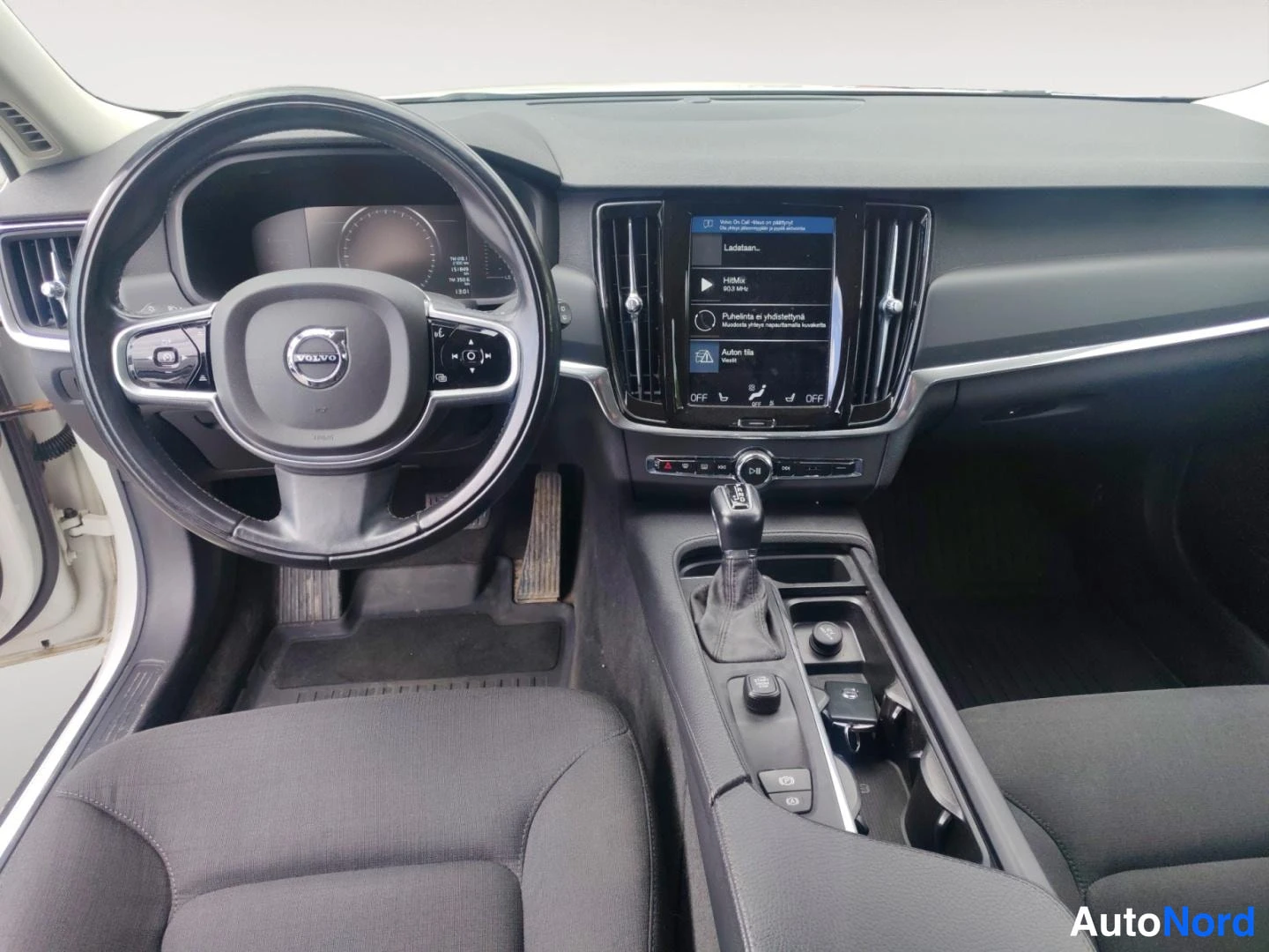 Muu: Volvo-merkkisen ohjauspyörän ja kosketusnäytön näkymä tummassa matkustamossa.