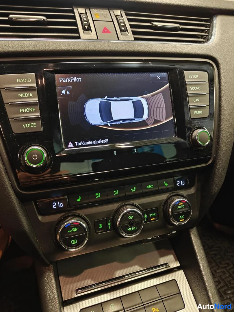 Muu: Auton kojelaudan keskikonsoli: infotainment-näyttö näyttää ParkPilot-törmäysvaroitusta ja tekstiä 'Tarkkaile ajotietä!'. Alla lämpötilanäytöt 21° ja ilmastoinni