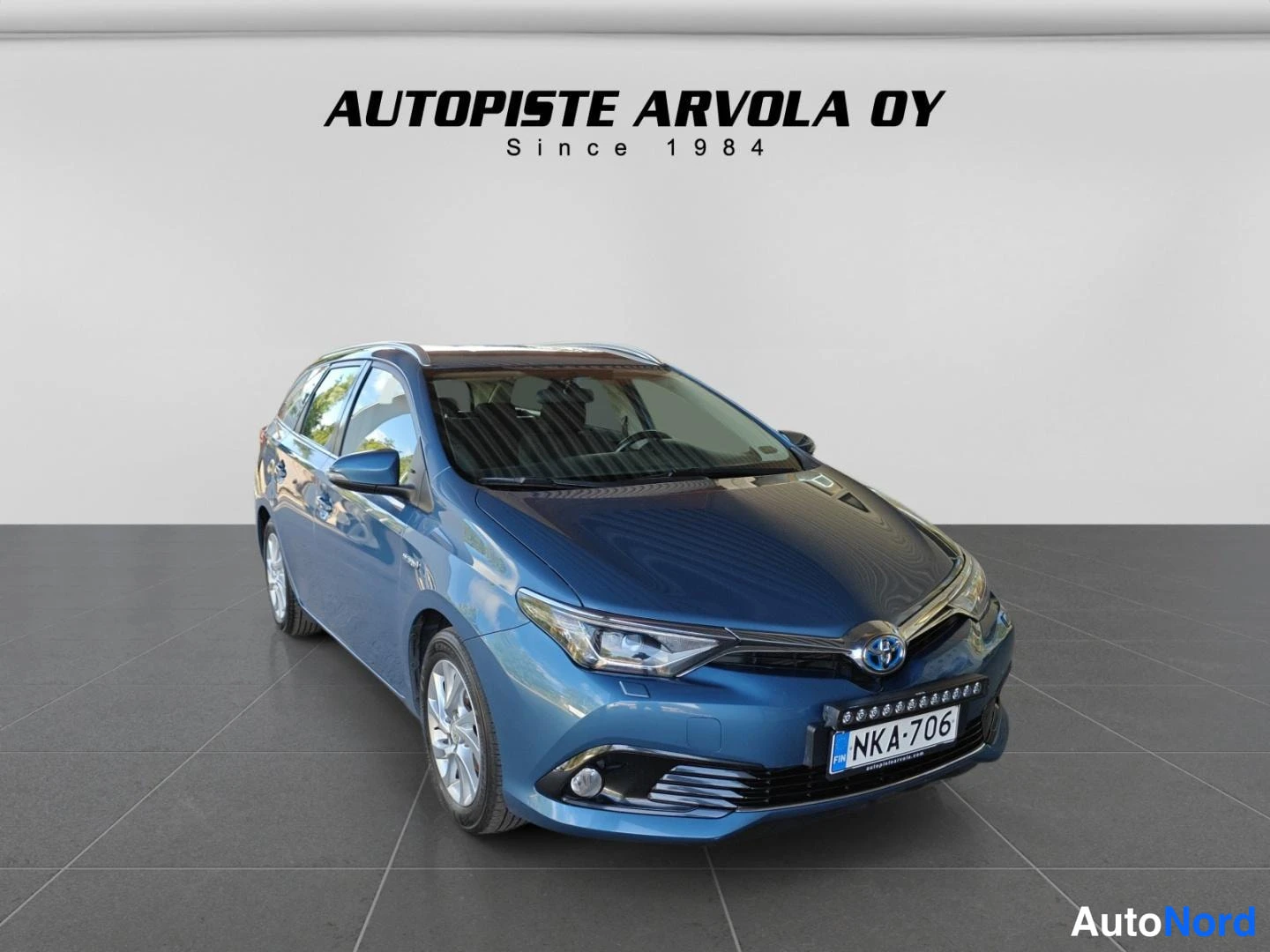 Etuviisto, nokka oikealle: Toyota Auris Touring Sports farmari vaalean sinertävän sinisenä etukulmasta; etusäleikkö ja Toyota-merkki näkyvät, rekisterikilpi, kuvassa myyjän logo Au