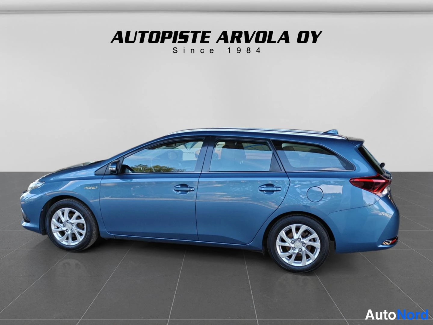 Sivulta: Sama farmarikorinen auto sivusta; sininen koripelti, konepellin Takamerkki HYBRIDSYNERGYDRIVE, takaosan autotarvikkeet, peilit ja takavalo näkyvät.