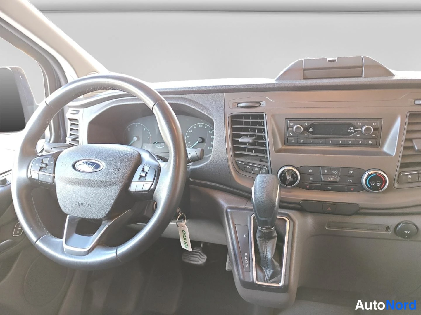 Muu: Ford-pakettiauton ohjaamo: monitoimiohjauspyörä, automaattivaihteen valitsin (P R N D M), radio ja A/C-painikkeet.