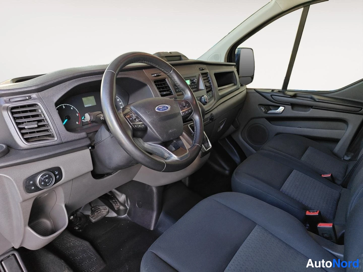Etuistuimet: Ford Transit Customin ohjaamo vasemmalta: monitoimiohjauspyörä Ford-logolla, kojetaulu, kaksi erillistä etuistuinta ja kaasupolvi.